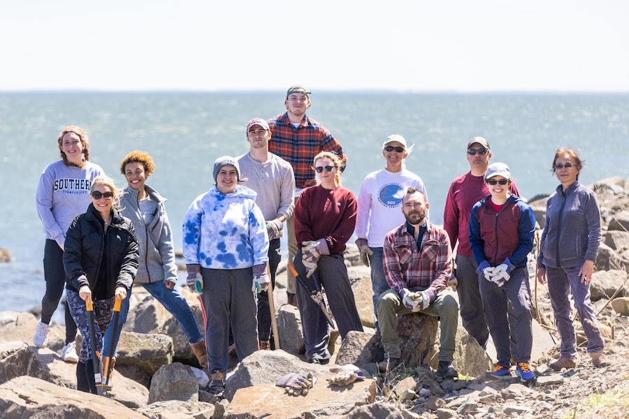 A group of students and faculty with the ocean in the background