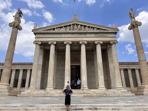 A woman standing in front of an ancient Greek building