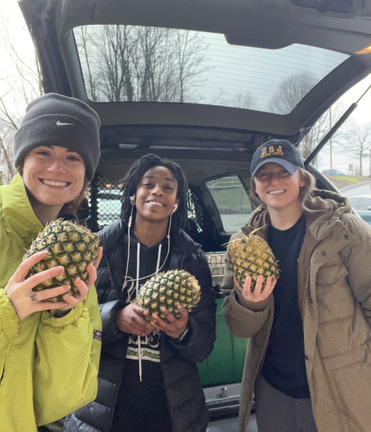 Three students at a food drive holding pineapples