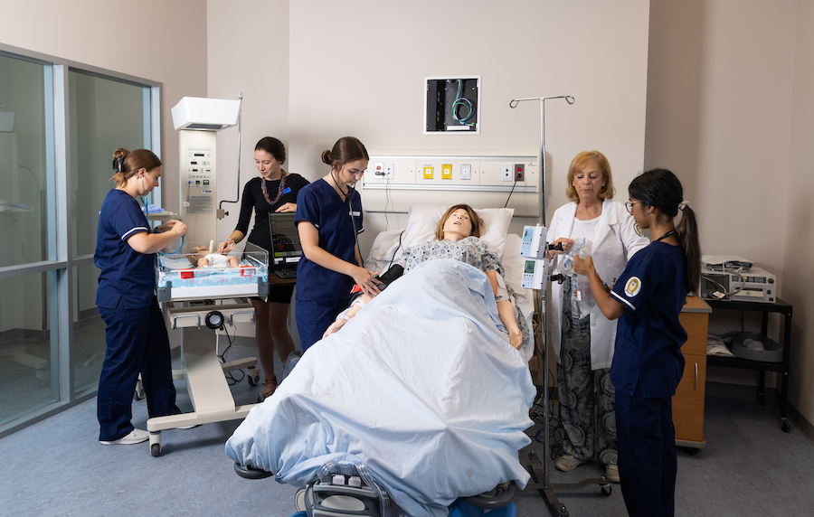 ""Nursing students practice medical techniques on a simulation doll under the supervision of nursing faculty.