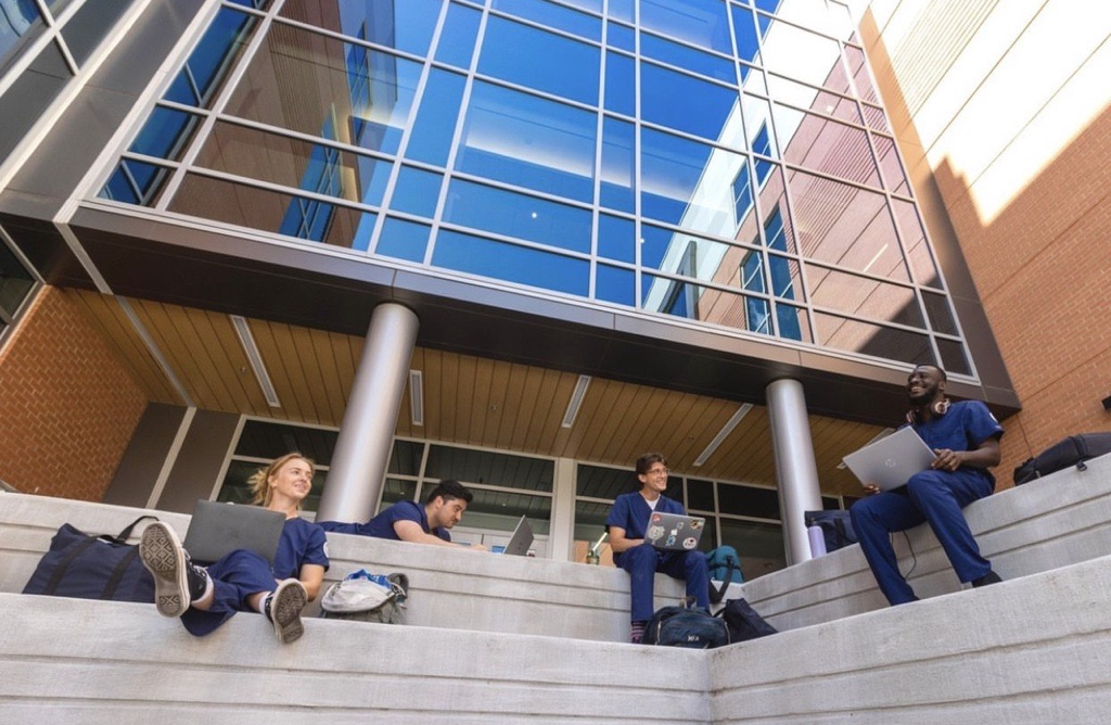 A group of students outside an academic building, studying and conversing