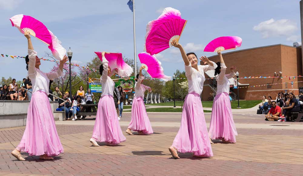 A group of dancers in traditional costume dancing outside an academic quad