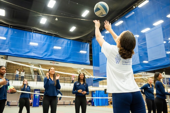 Young girl hitting a volley ball with SCSU women's volley ball team cheering her on