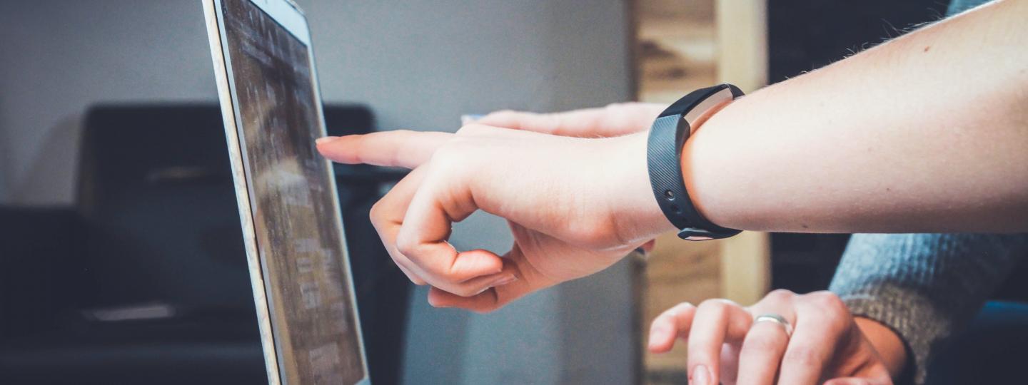 decorative image of the hands of two people pointing at the screen of a laptop