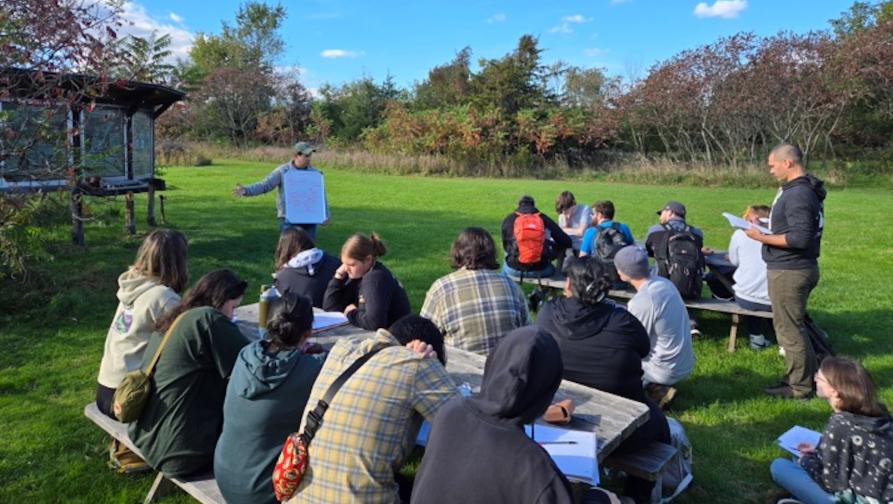 A group of Earth Science students sitting at benches and being given a presentation at the SCSU Garden