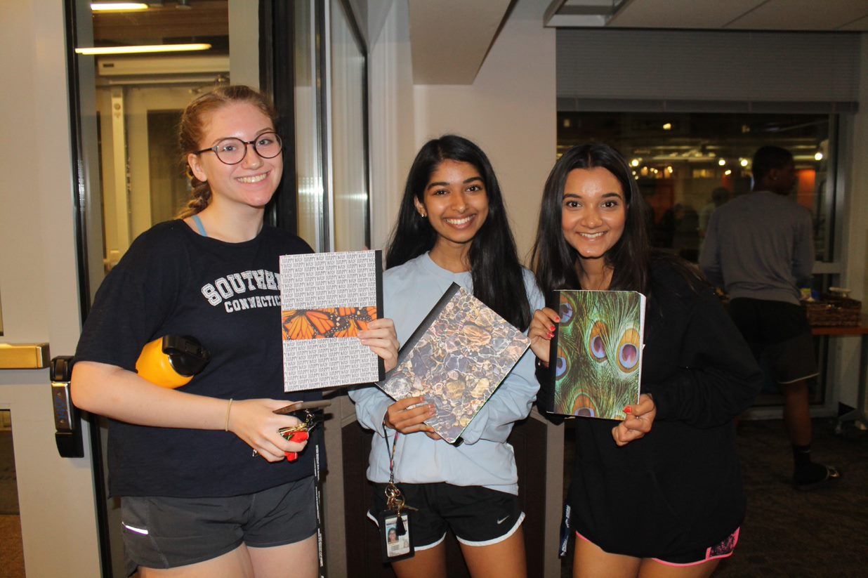 Three students, each holding a notebook