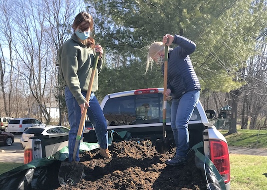 Two workers shoveling dirt from a truck bed into the SCSU Garden.