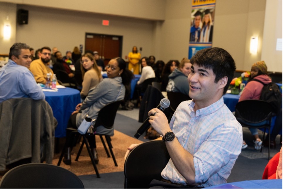 A student in the audience of an event speaking into a microphone.